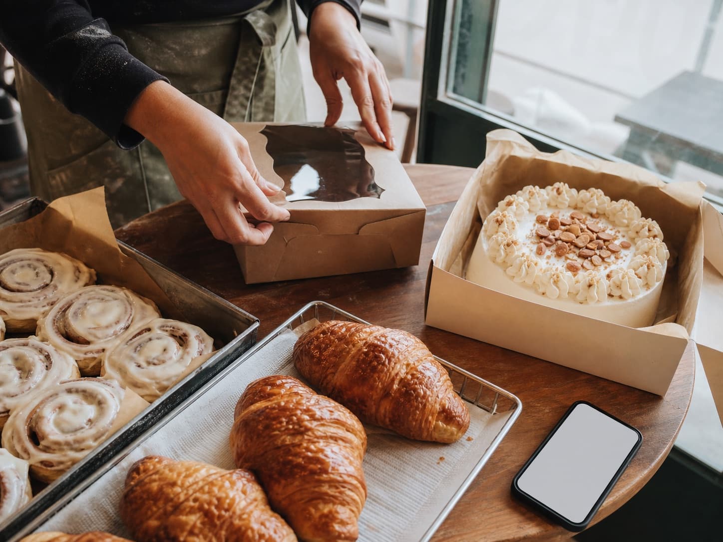 A baker packing pastries and a finished cake for pickup